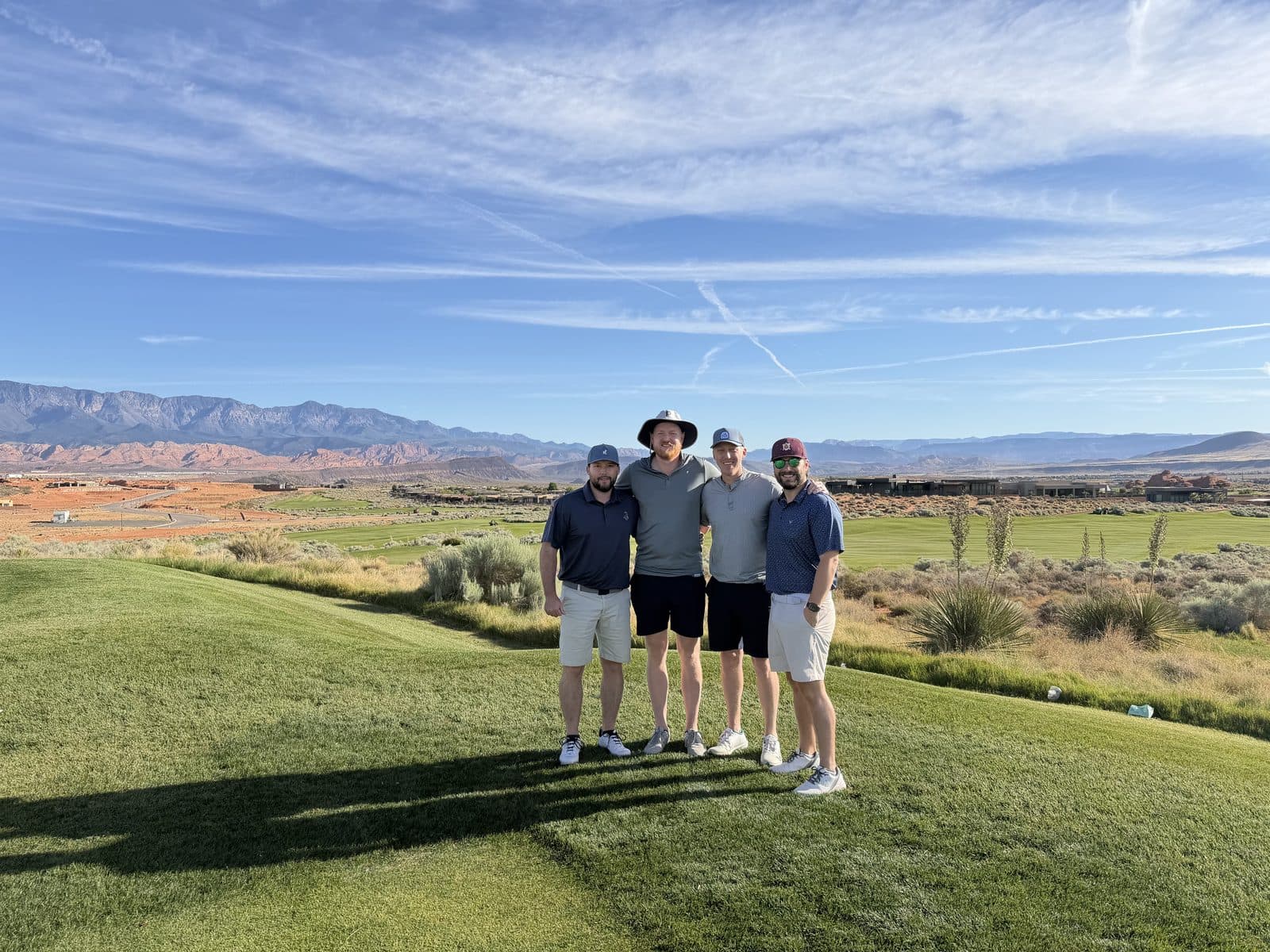 Four golfers standing together on a desert golf course.