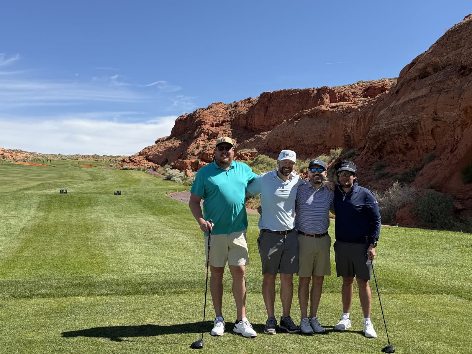 A foursome standing on a fairway bordered by red rock.
